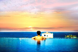 A person in a swimming pool with a sunset and a distant building. - ANFADA Hotel Danang (Da Nang)