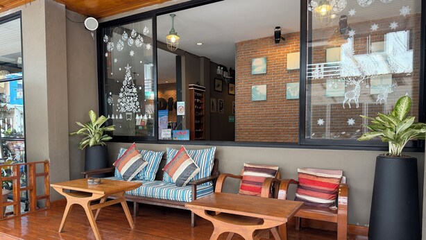 Un coin salon accueillant avec un canapé et deux tables en bois, une grande plante en pot et un mur de briques orné de tableaux.