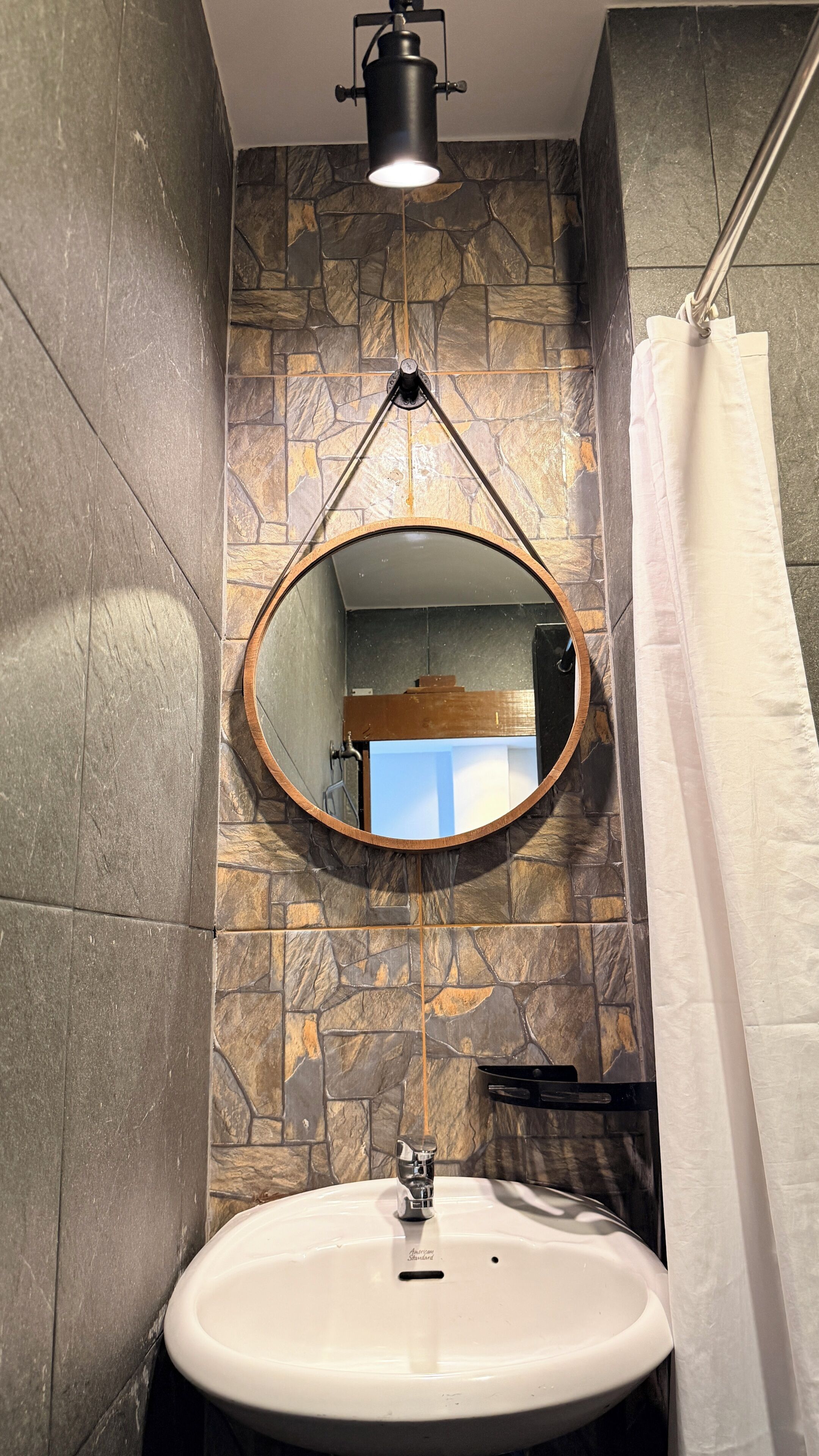 A bathroom with a white sink, a round mirror, and a shower curtain.