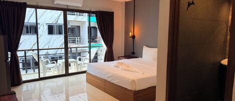 A hotel room with a bed, a nightstand, a lamp, a window with curtains, and a view of the outside.