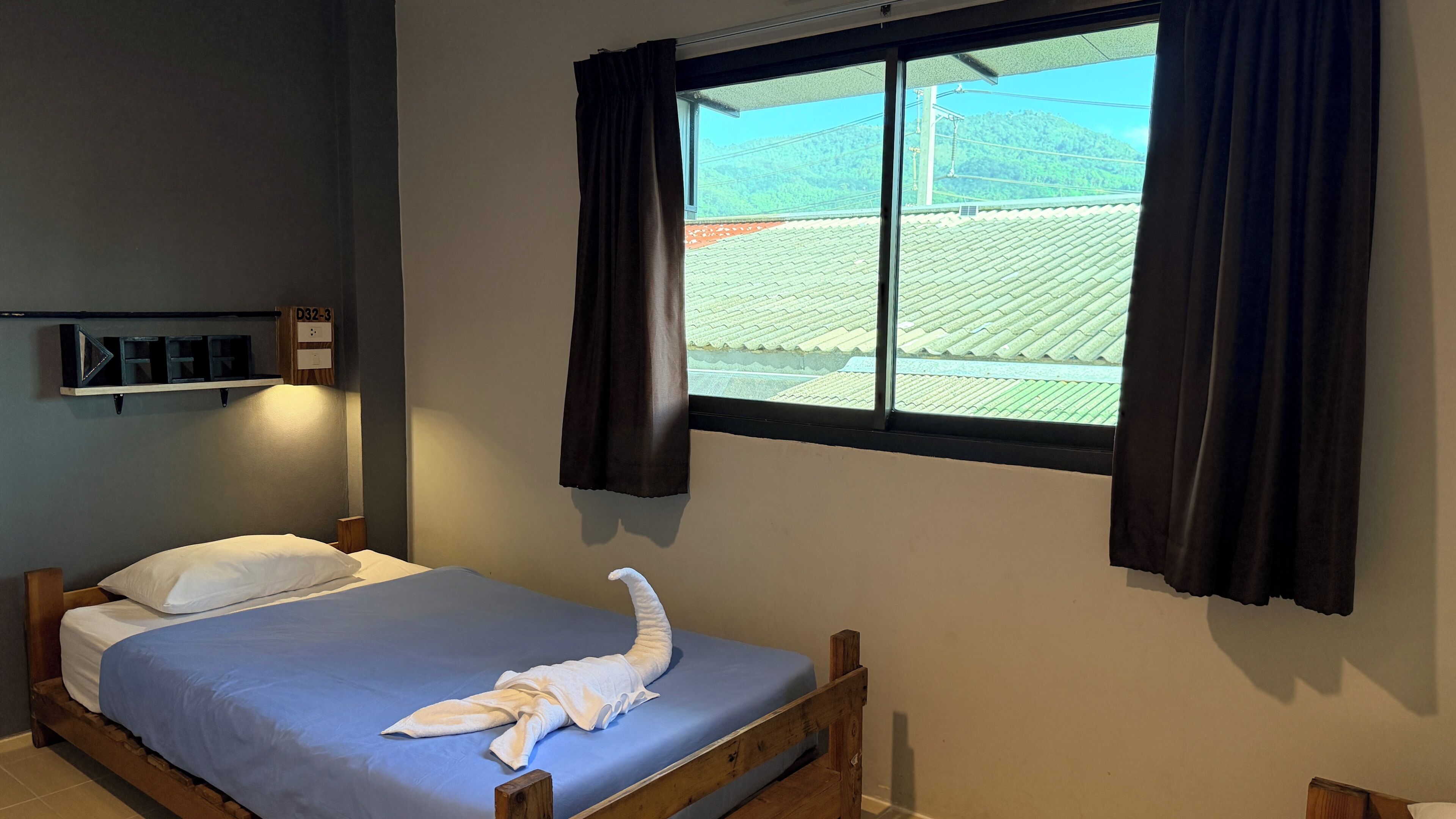 Un lit simple avec un matelas bleu, une tête de lit en bois et une serviette blanche pliée sur le lit.