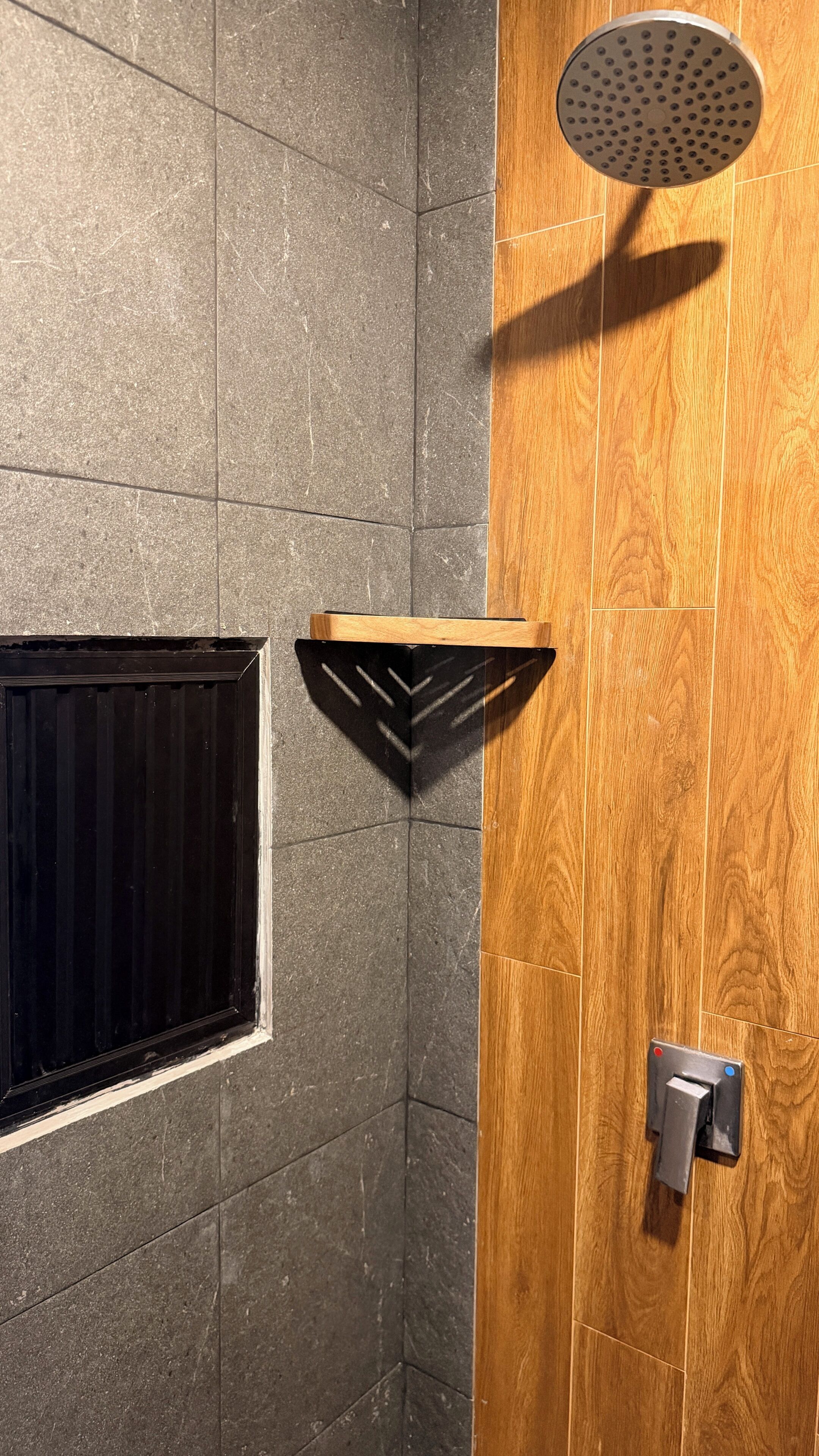 A shower area with a wooden door, a black shelf, and a showerhead.