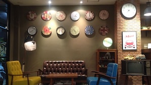 Une pièce avec un canapé en cuir marron, deux fauteuils, un mur en briques orné d’horloges et un téléviseur ancien.