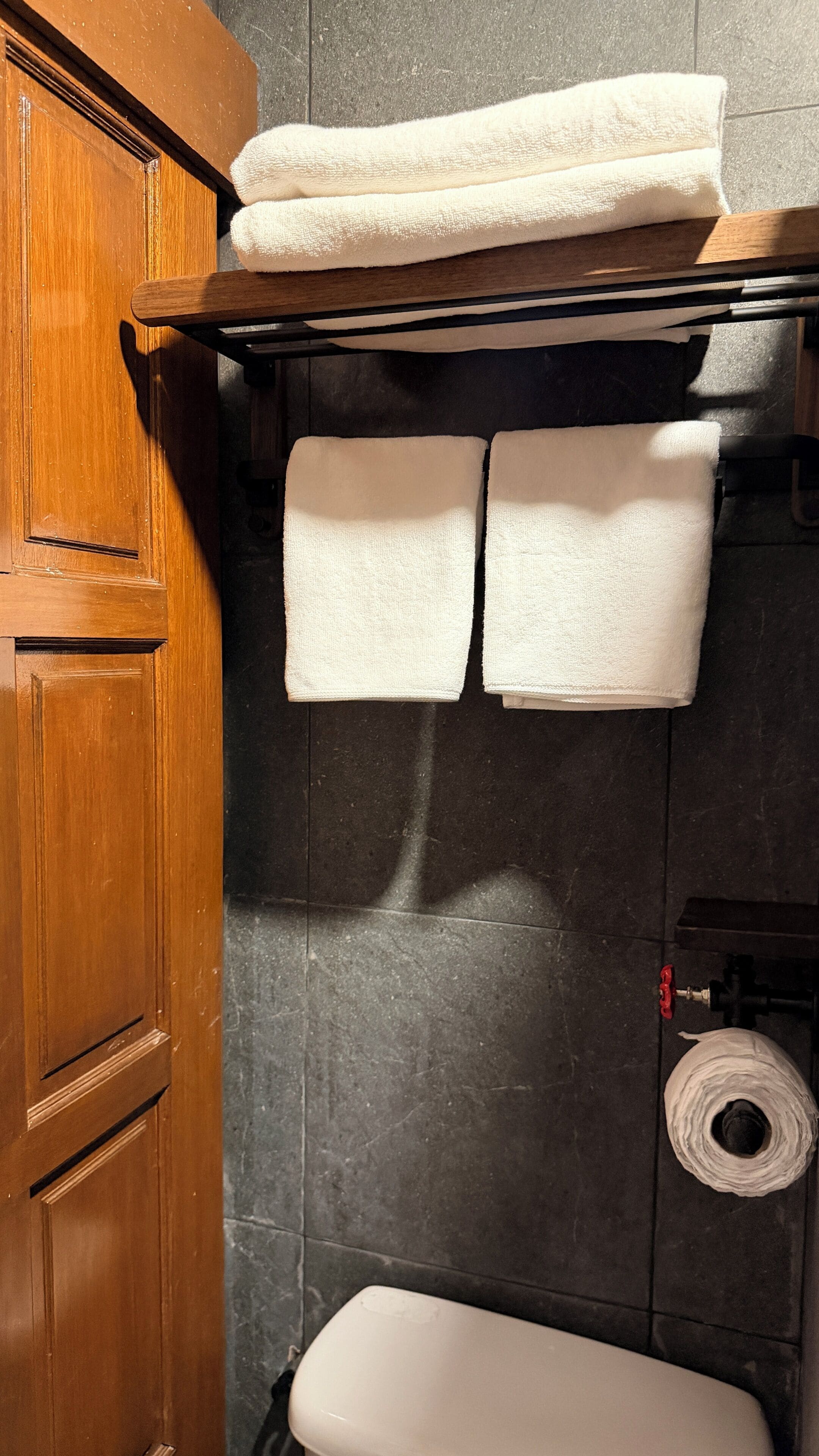 Ein Badezimmer mit Holztür, Handtuchhalter mit zwei Handtüchern, Toilette und Toilettenpapierrolle.
