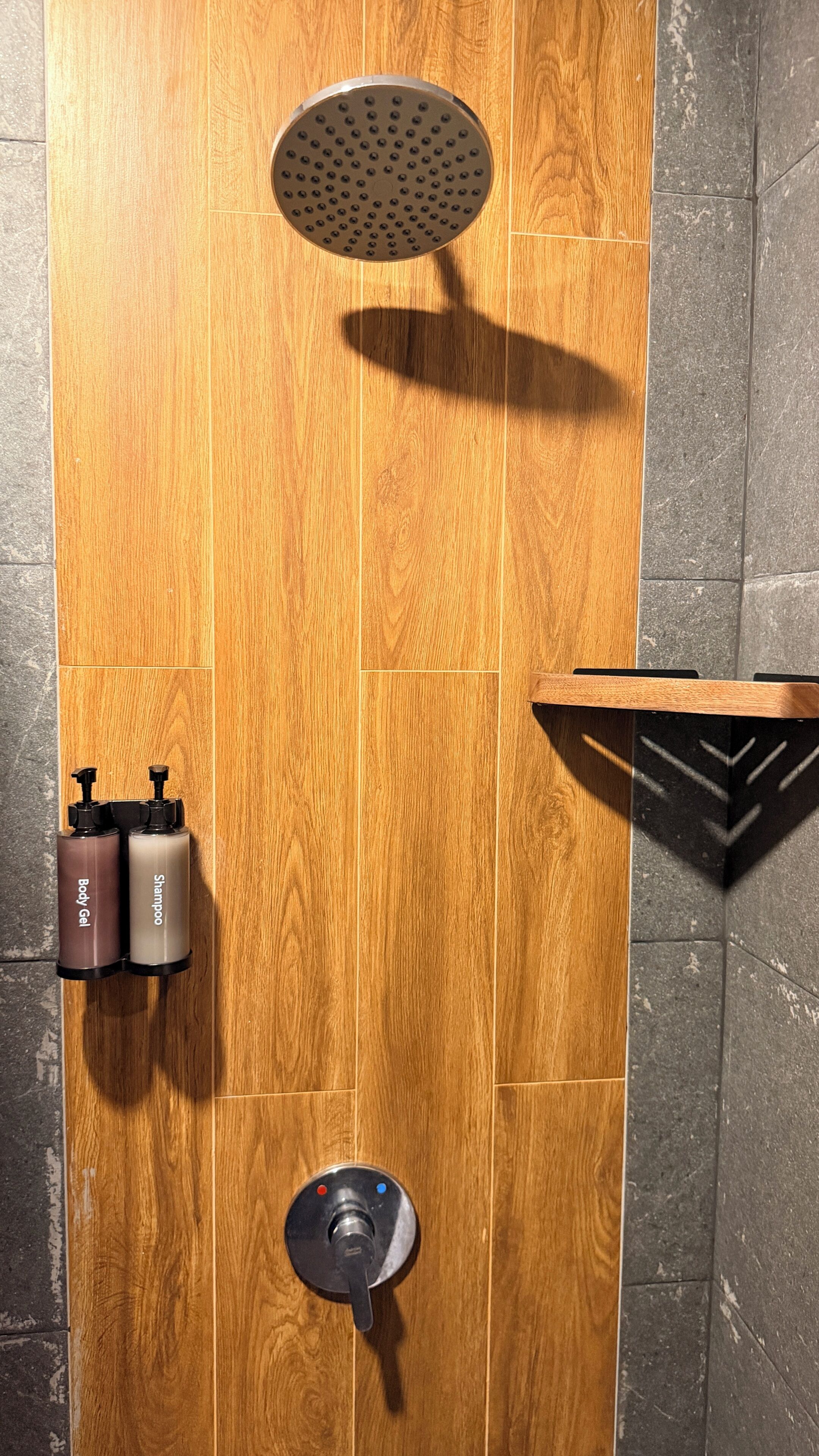 A shower with a wooden panel wall, a handheld showerhead, and two bottles of shampoo and body gel.