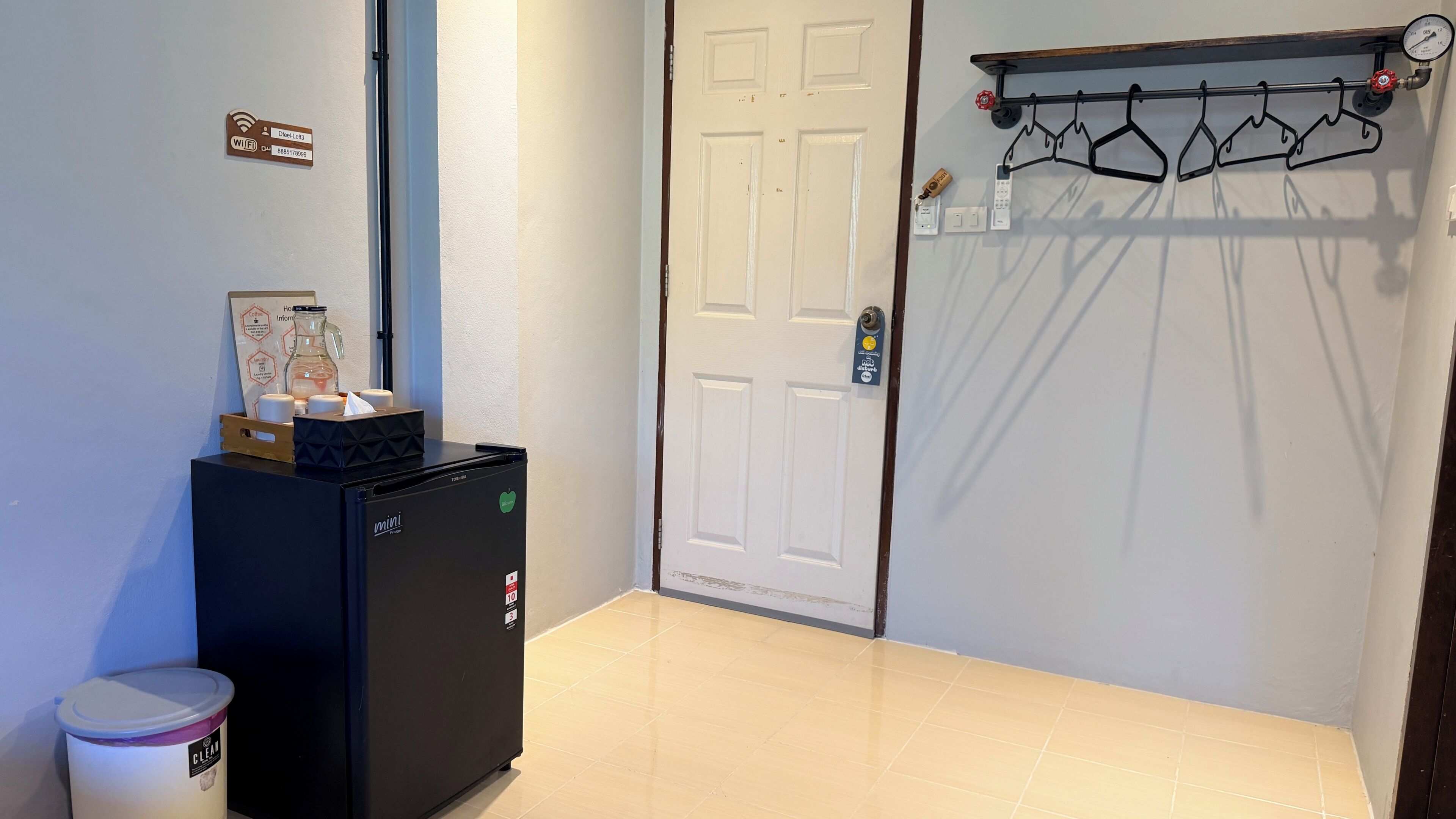 A clean, well-lit hallway with a refrigerator, a door with a coat rack, and a trash bin.