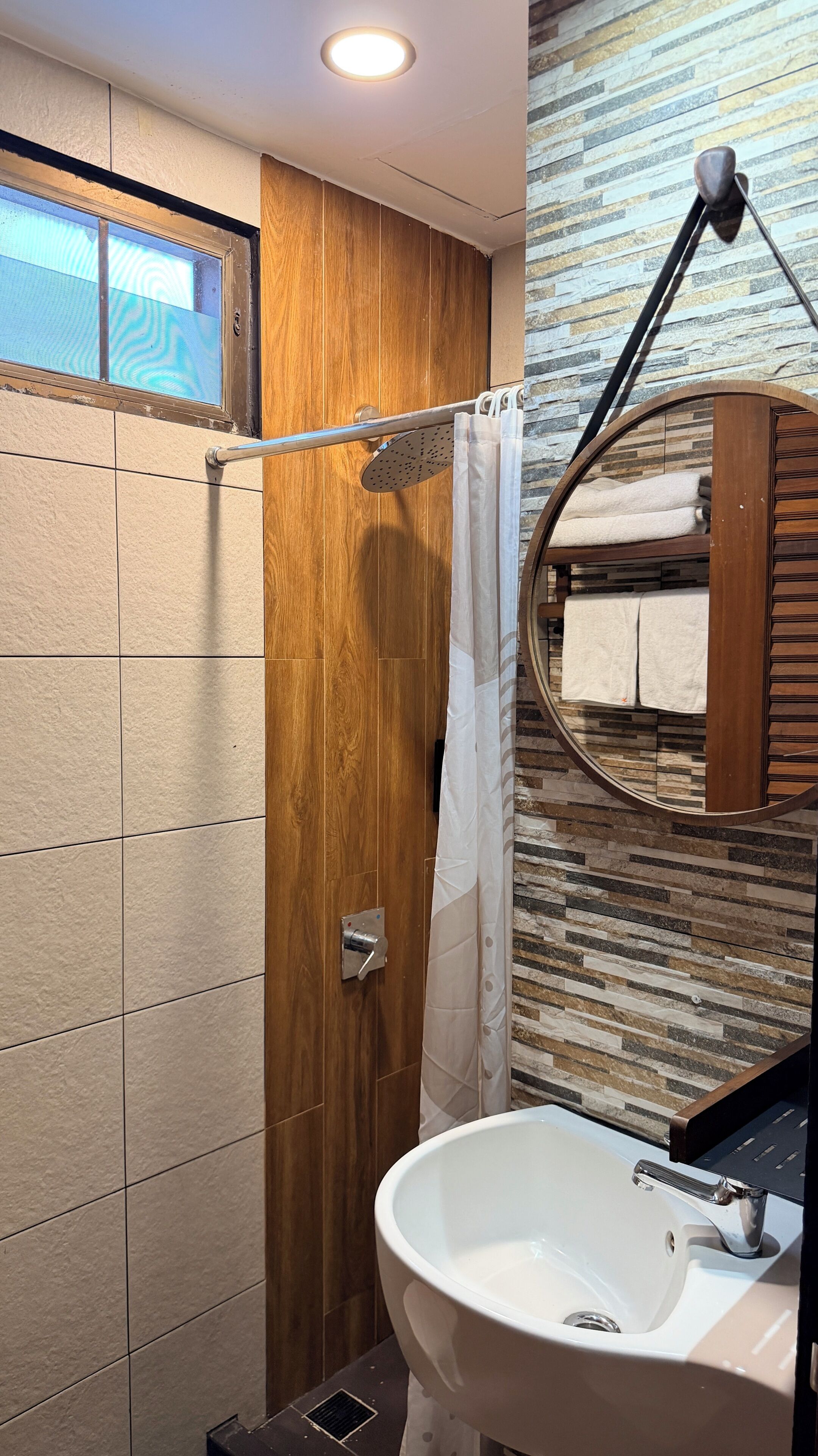 A bathroom with a wooden wall, a shower curtain, a sink, and a mirror.
