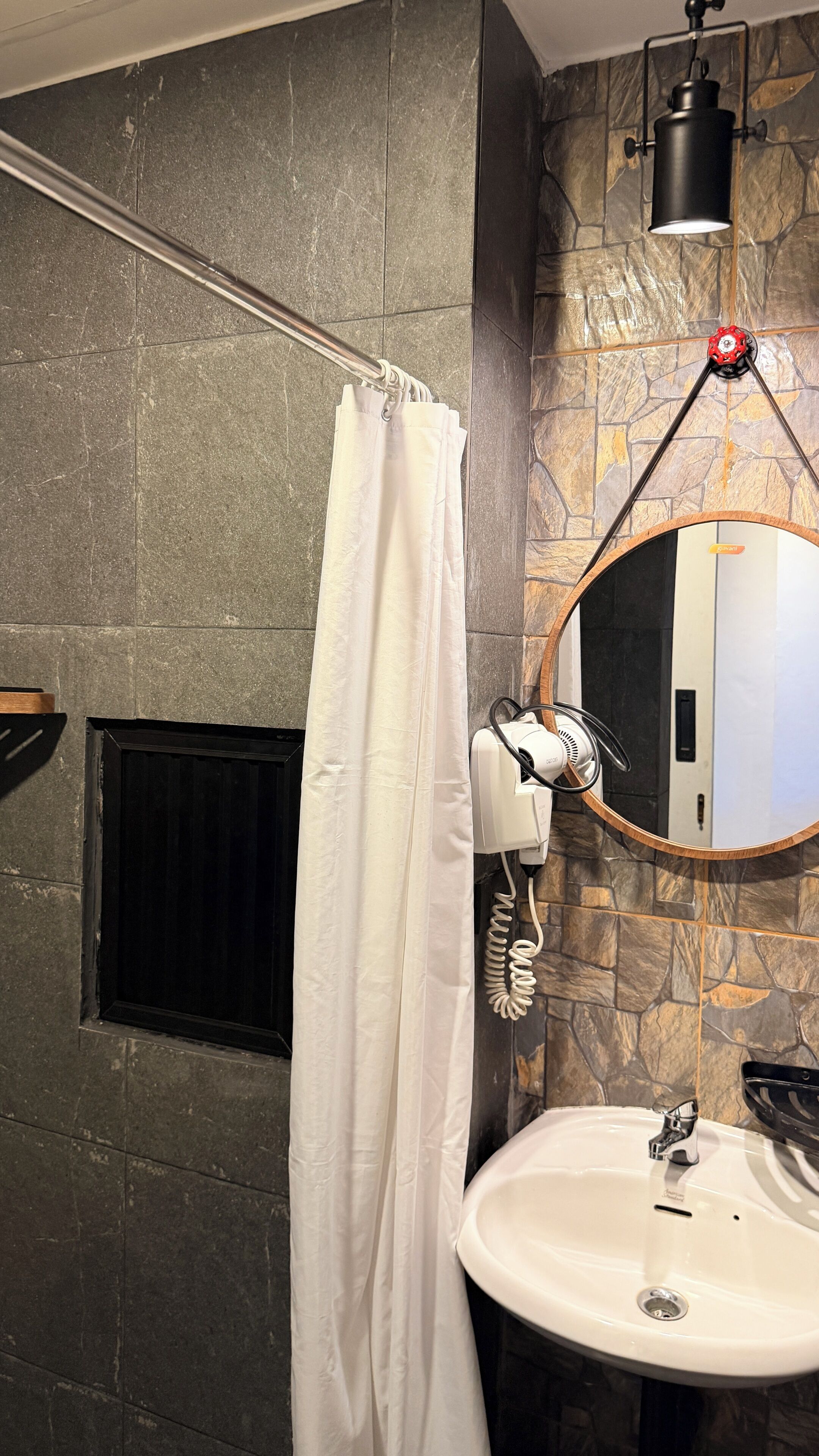 A bathroom with a white shower curtain, a round mirror with a wooden frame, a white sink, and a towel rack.