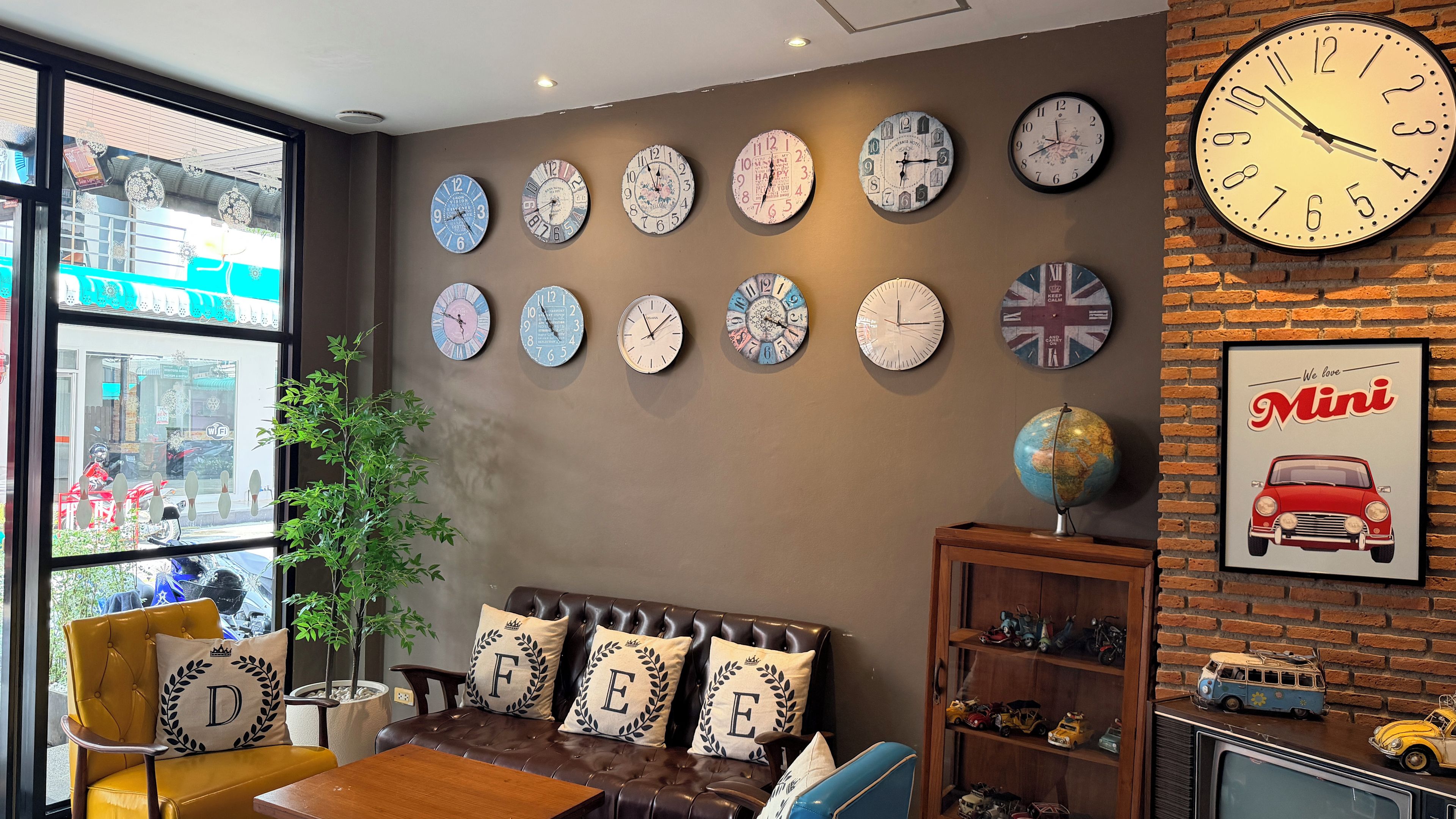 A room with a brown leather sofa, multiple wall clocks, a globe, and a brick wall.