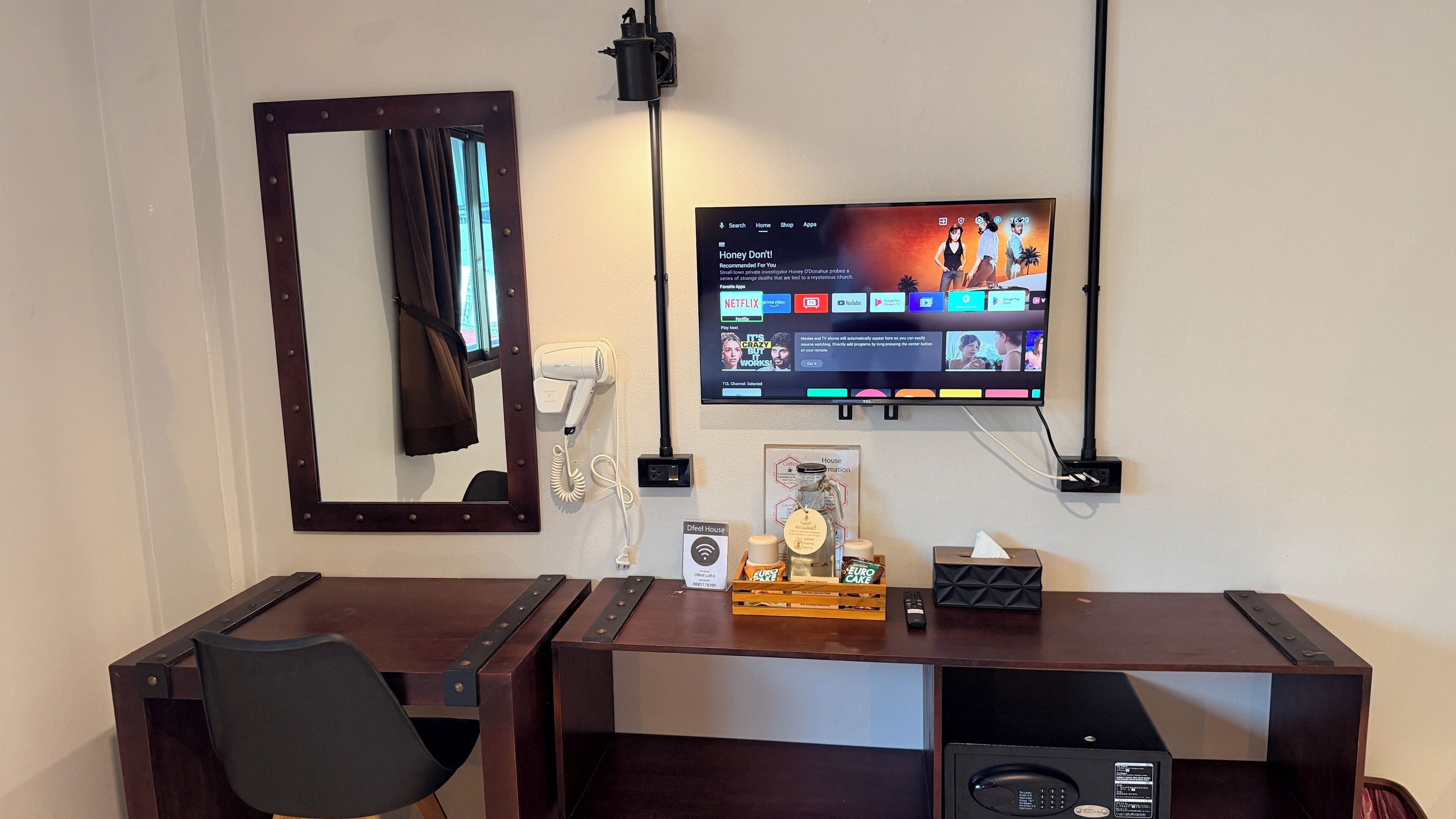 A hotel room with a desk, chair, TV, and a mirror.