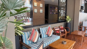A cozy seating area with a sofa and chairs, a wooden table, and large windows with artwork. - Dfeel House (Patong)