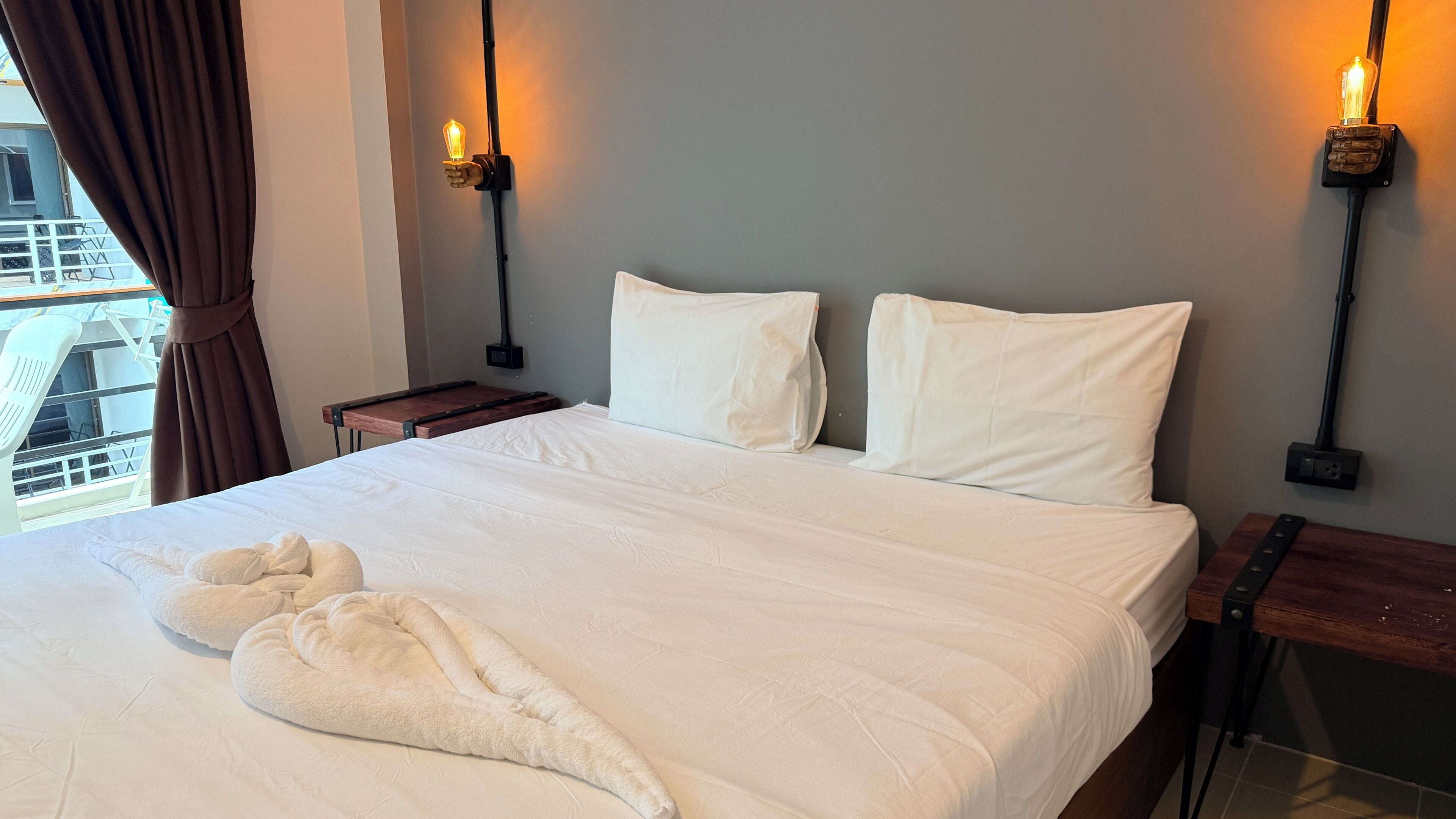 Habitación de hotel con una cama grande, dos mesitas de noche, una ventana con cortinas y vistas a un edificio.