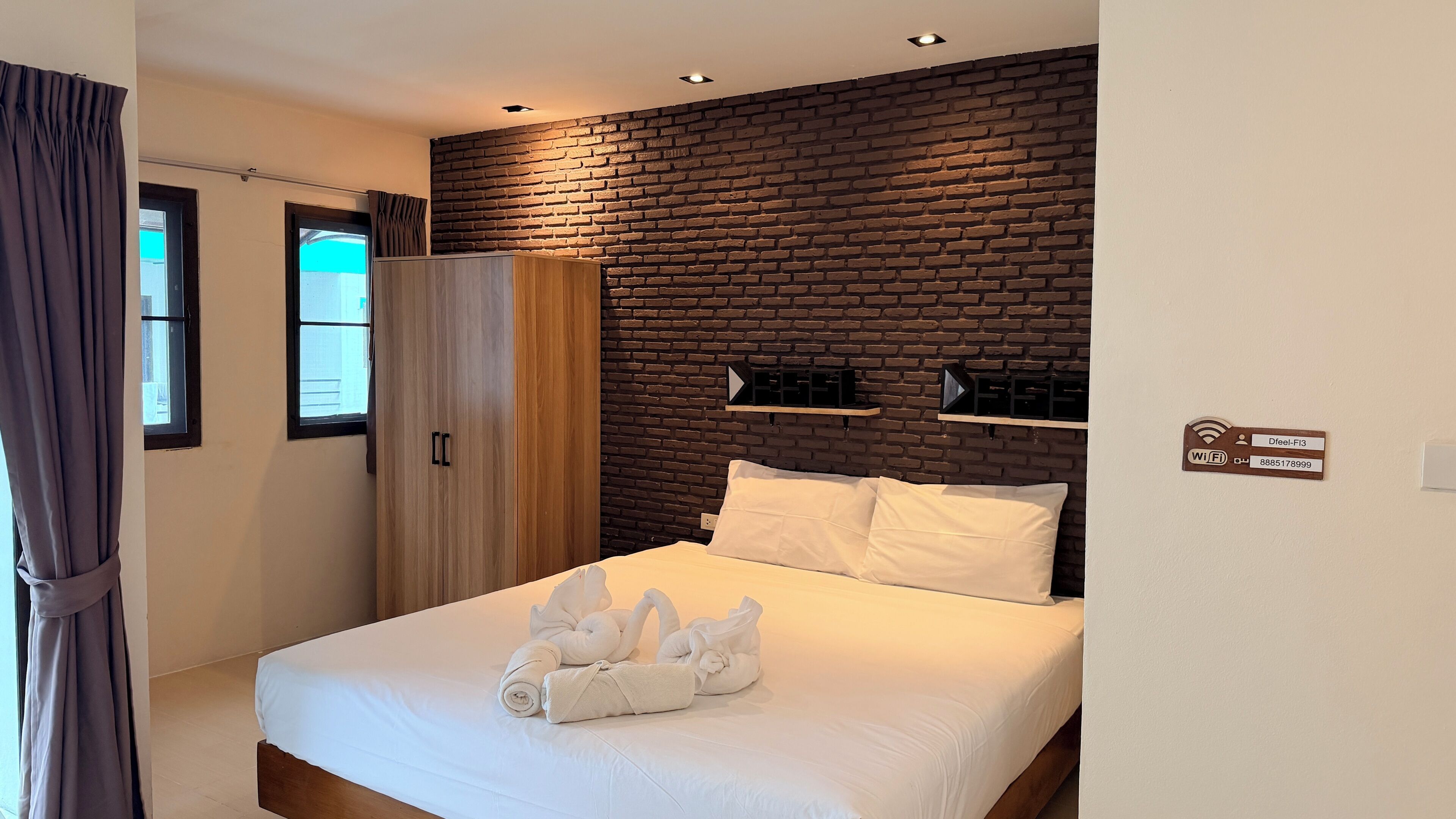 Habitación de hotel con pared de ladrillo, cama con ropa blanca, armario y señal de Wi-Fi.