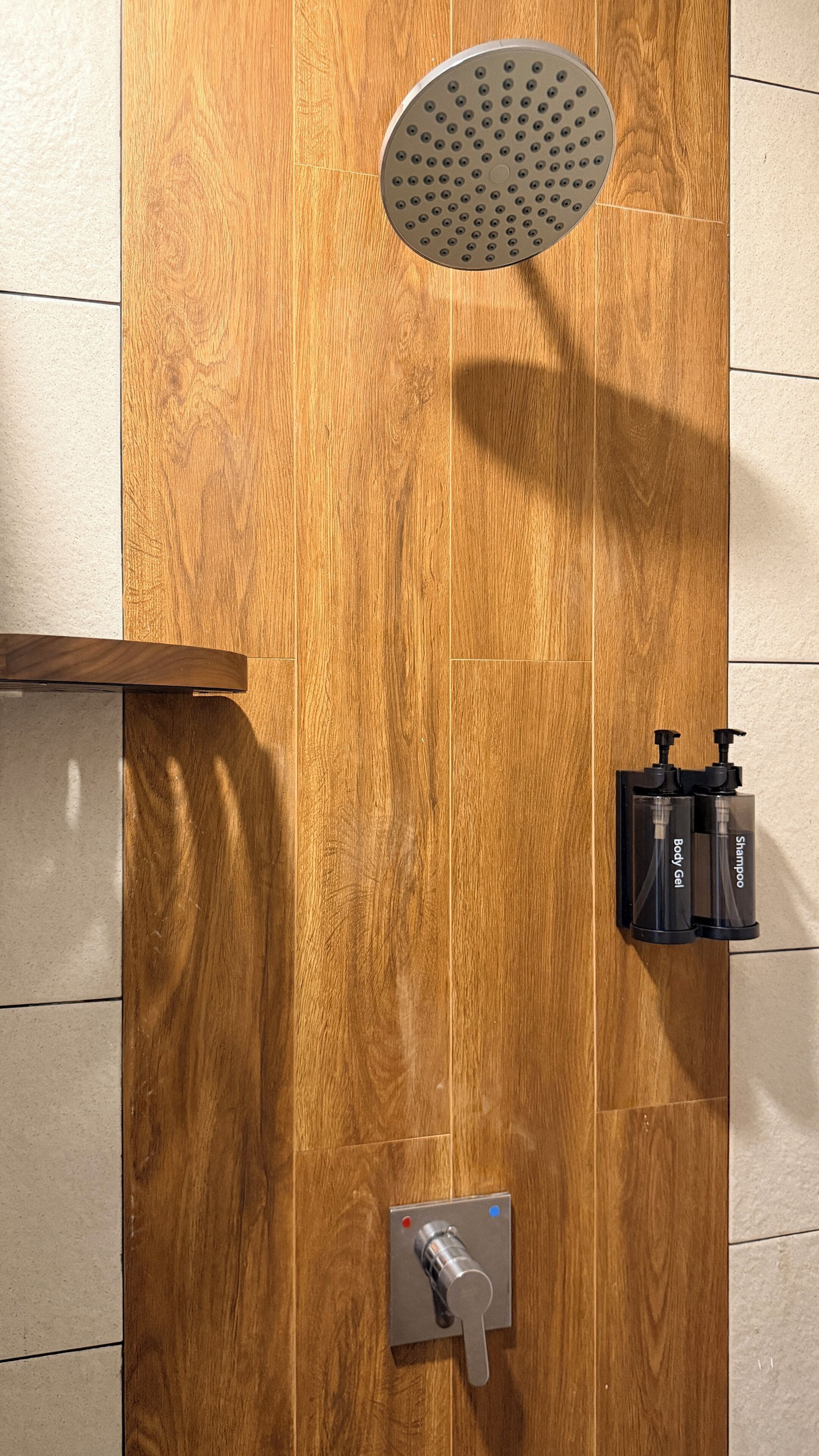 A wooden shower enclosure with a handheld showerhead, a soap dispenser, and a control knob.