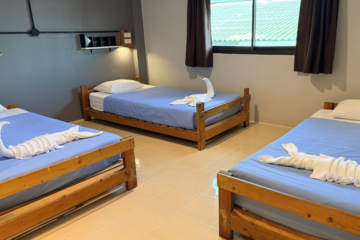 A hotel room with two wooden beds, each with a blue bedspread and a white towel arranged in a decorative manner.