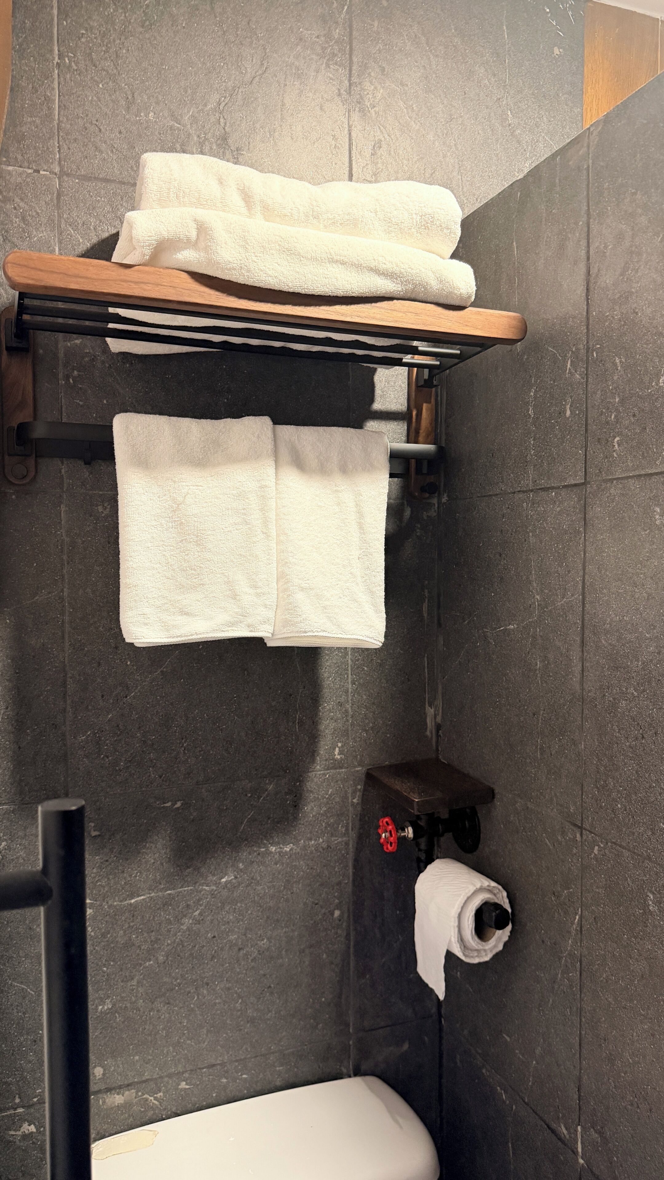 Ein Badezimmer mit Toilette, einem Handtuchhalter mit zwei Handtüchern und einer Holzablage.