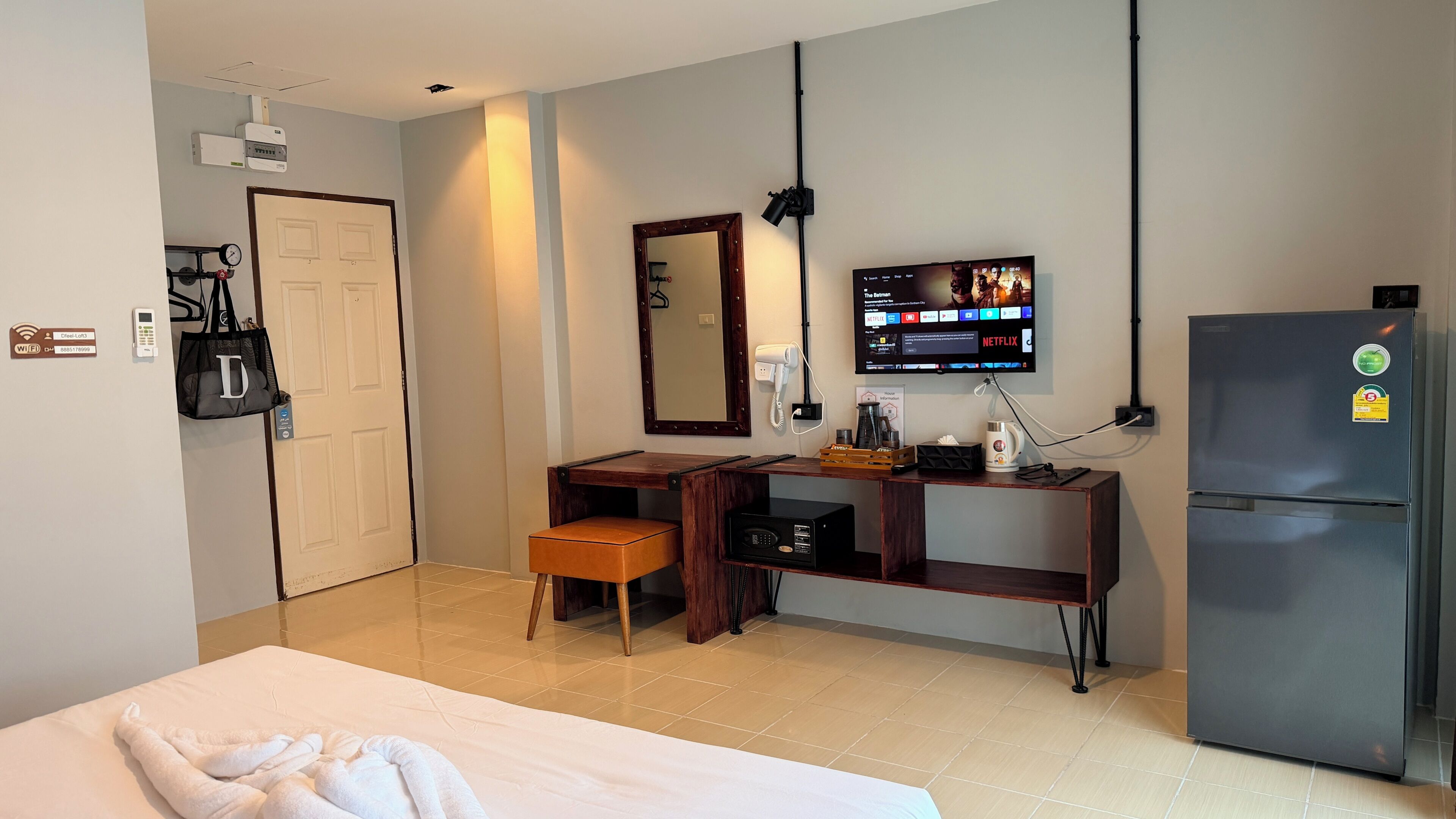 A hotel room with a bed, a desk with a chair, a refrigerator, a TV mounted on the wall, and a bathroom door.
