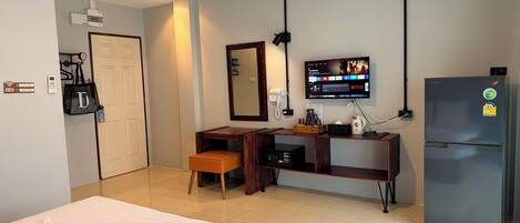 A hotel room with a bed, a desk with a chair, a refrigerator, a TV mounted on the wall, and a bathroom door.