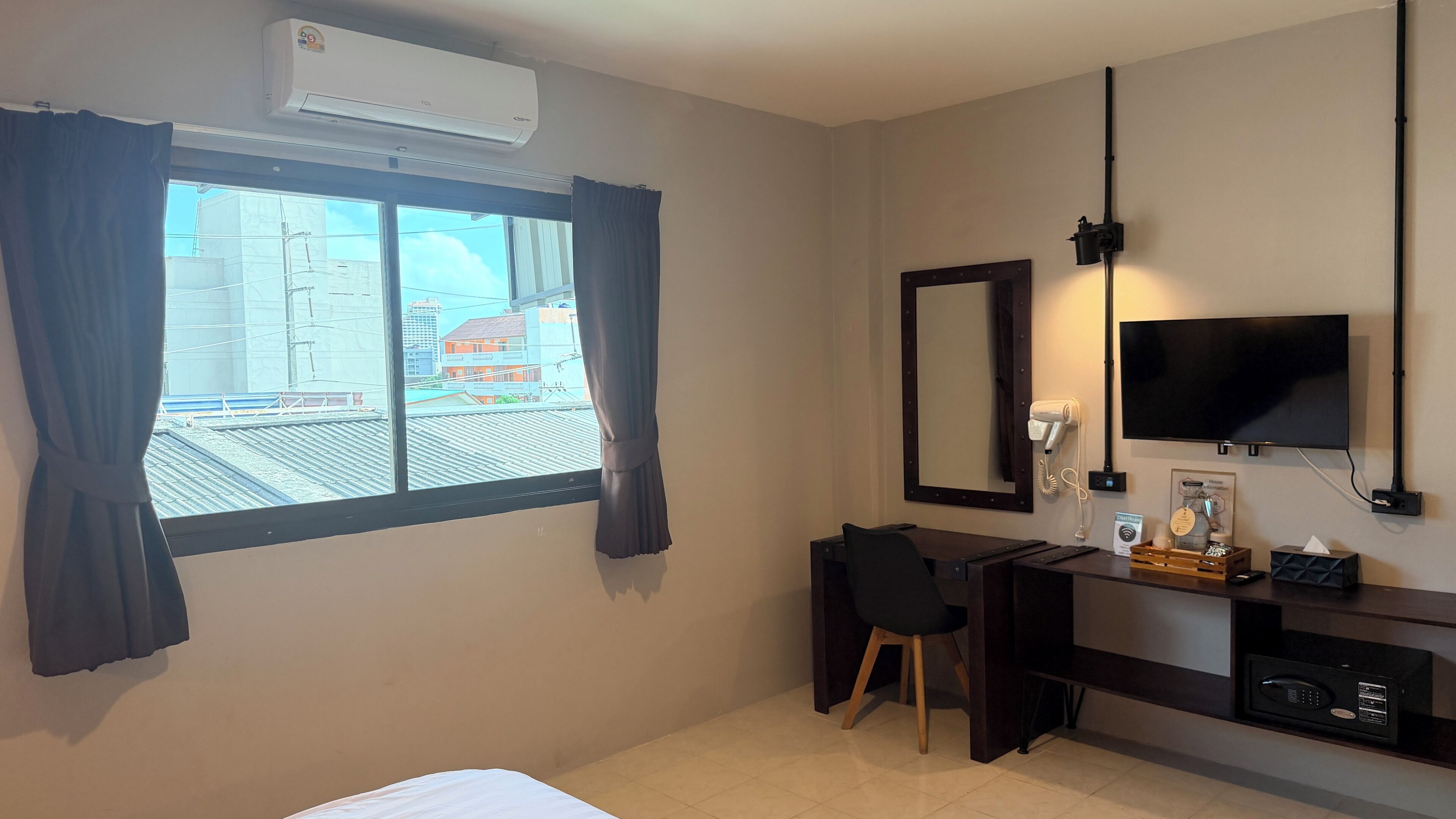 Habitación de hotel con cama, escritorio, silla, televisor, secador de pelo y espejo.