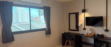 Habitación de hotel con cama, escritorio, silla, televisor, secador de pelo y espejo.