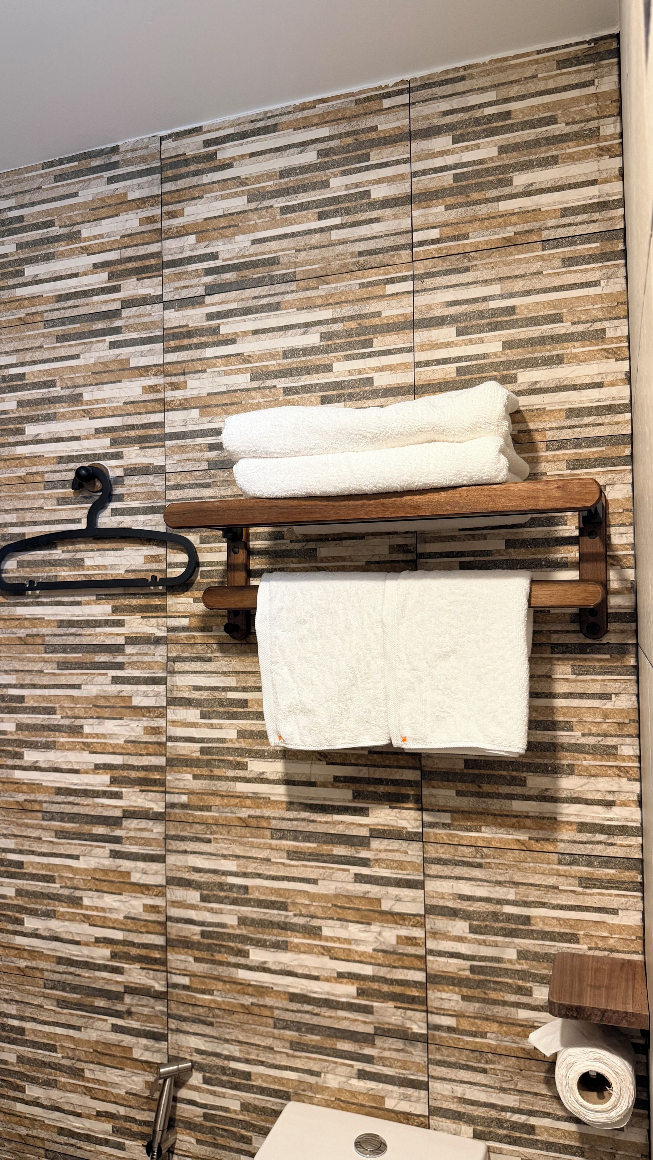 A bathroom with a wooden towel rack, a towel hanging, and a toilet paper roll.