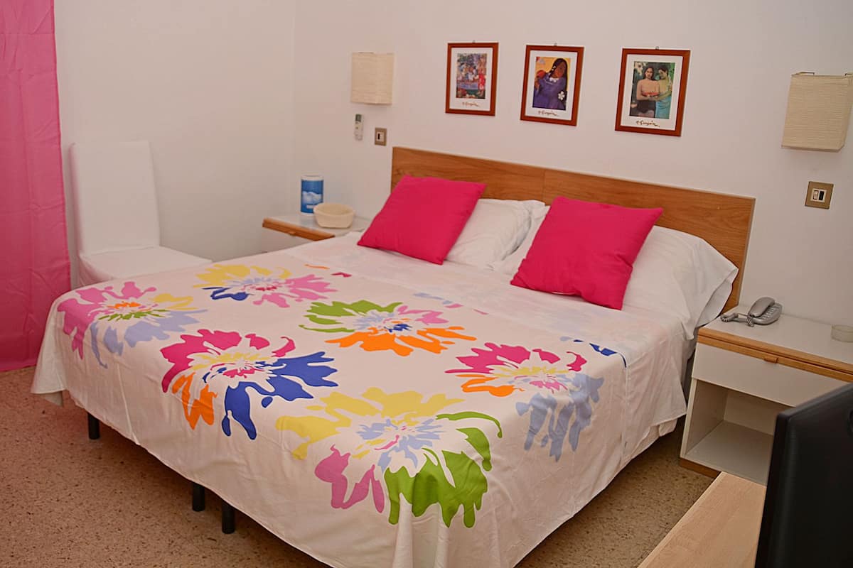 A bed with a colorful floral bedspread, two pink pillows, and a wooden headboard. There are three framed pictures on the wall above the bed.