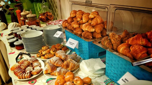 Un buffet proposant une variété de viennoiseries et de desserts, notamment des croissants et des pains au chocolat, disposés sur une table avec des assiettes et des ustensiles de service.