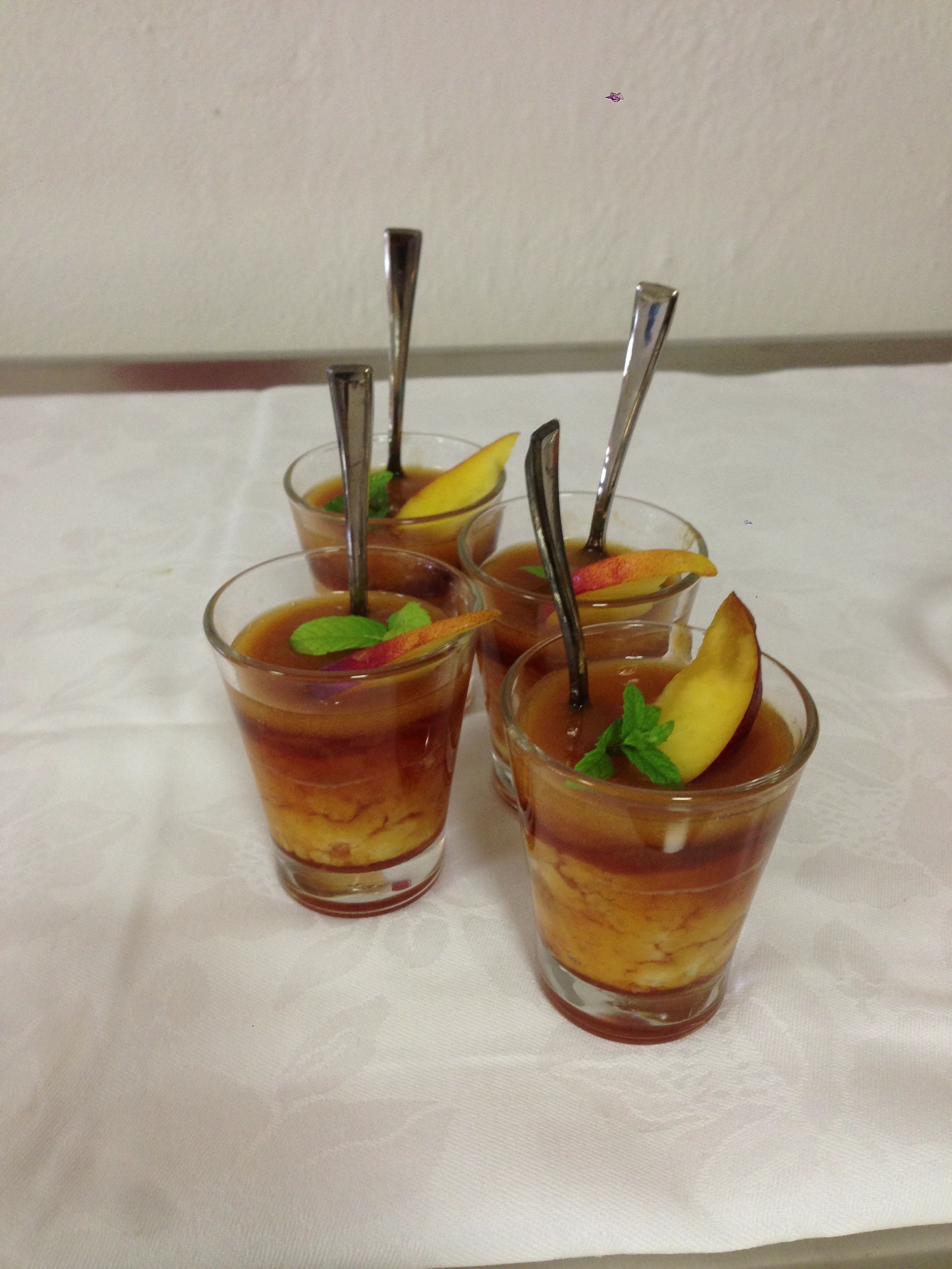 Quattro bicchieri di una bevanda a strati con fette di frutta e foglie di menta, ognuno con un cucchiaino.