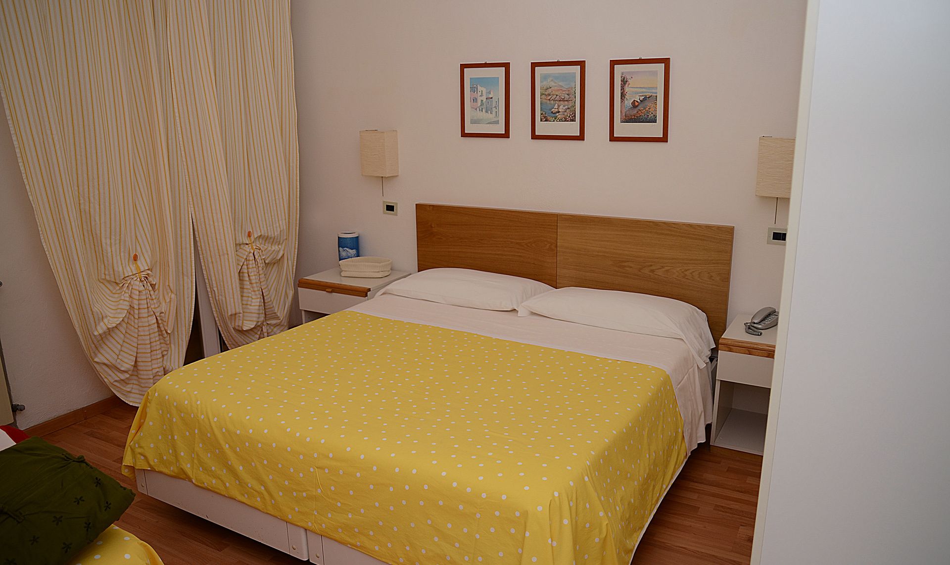 Ein Hotelzimmer mit einem Bett, einem Nachttisch, einem Telefon und drei gerahmten Bildern an der Wand.