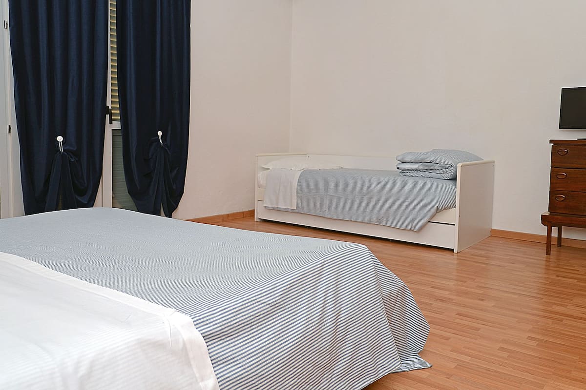 A bedroom with a bed, a small bedside table, a dresser, and a television.