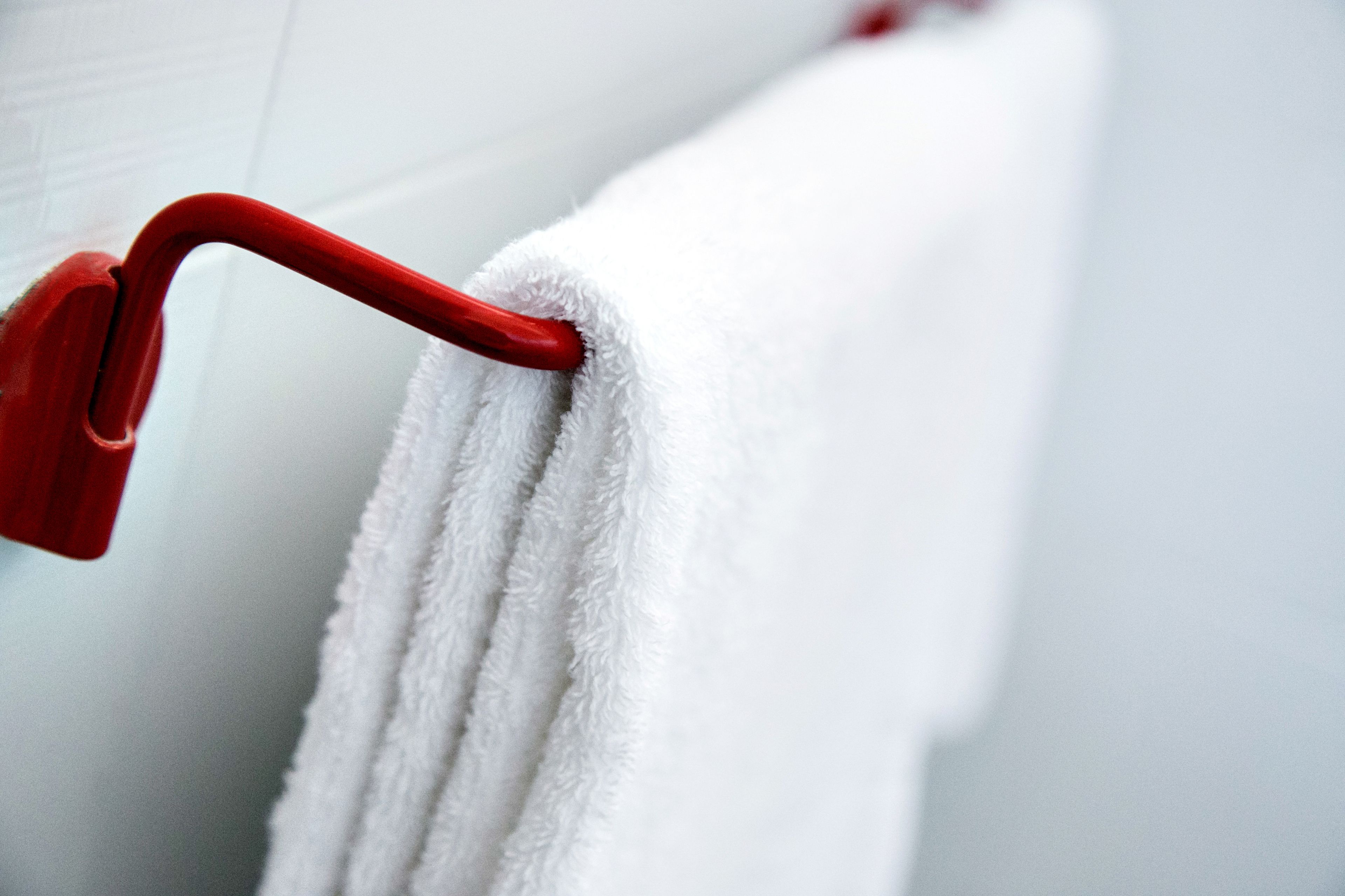 A white towel hanging on a red towel rack in a bathroom.