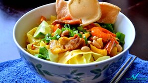 A bowl of noodle dish with vegetables and meat, accompanied by a piece of bread. - Huong Duy Hotel (Da Nang)