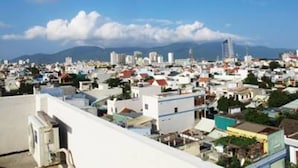 A cityscape with a mix of residential and commercial buildings, a clear blue sky, and distant mountains. - Huong Duy Hotel (Da Nang)
