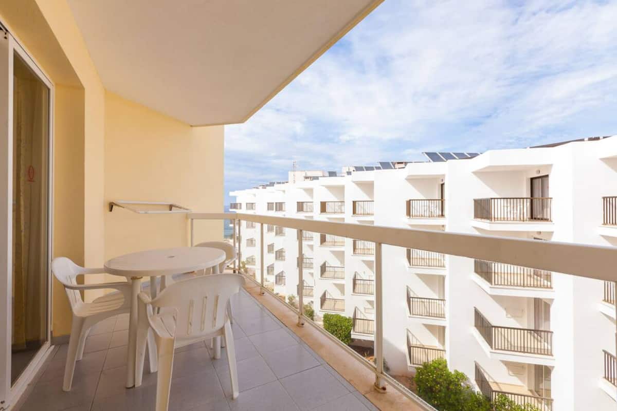 Ein Balkon mit Tisch und Stühlen, mit Blick auf eine Reihe weißer Apartmentgebäude mit Balkonen.