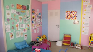 A colorful classroom with a blue couch, a table with a laptop and drinks, and various children's artwork on the walls. - Can Salia (Sant Josep de sa Talaia)