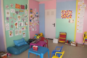 A colorful classroom with a blue couch, a table with a laptop and drinks, and various children's artwork on the walls. - Can Salia (Sant Josep de sa Talaia)