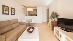A modern living room with a sofa, a coffee table with a bowl, a flat-screen TV, and a dining area with a table and chairs. - Can Salia (Sant Josep de sa Talaia)