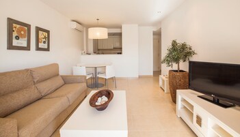Una sala de estar moderna con sofá, una mesa de centro con un cuenco, un televisor de pantalla plana y un comedor con mesa y sillas.