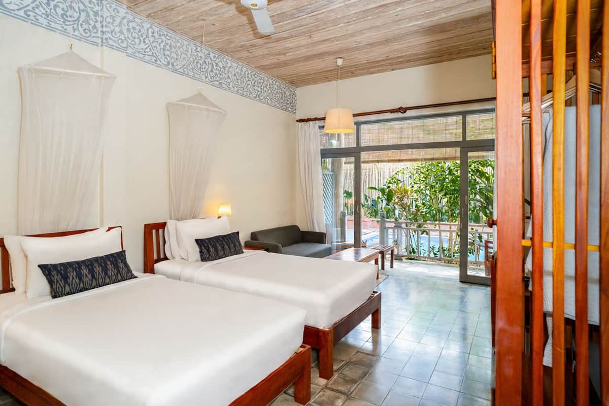 Une chambre d’hôtel avec deux lits, un balcon donnant sur un espace verdoyant et un ventilateur de plafond.