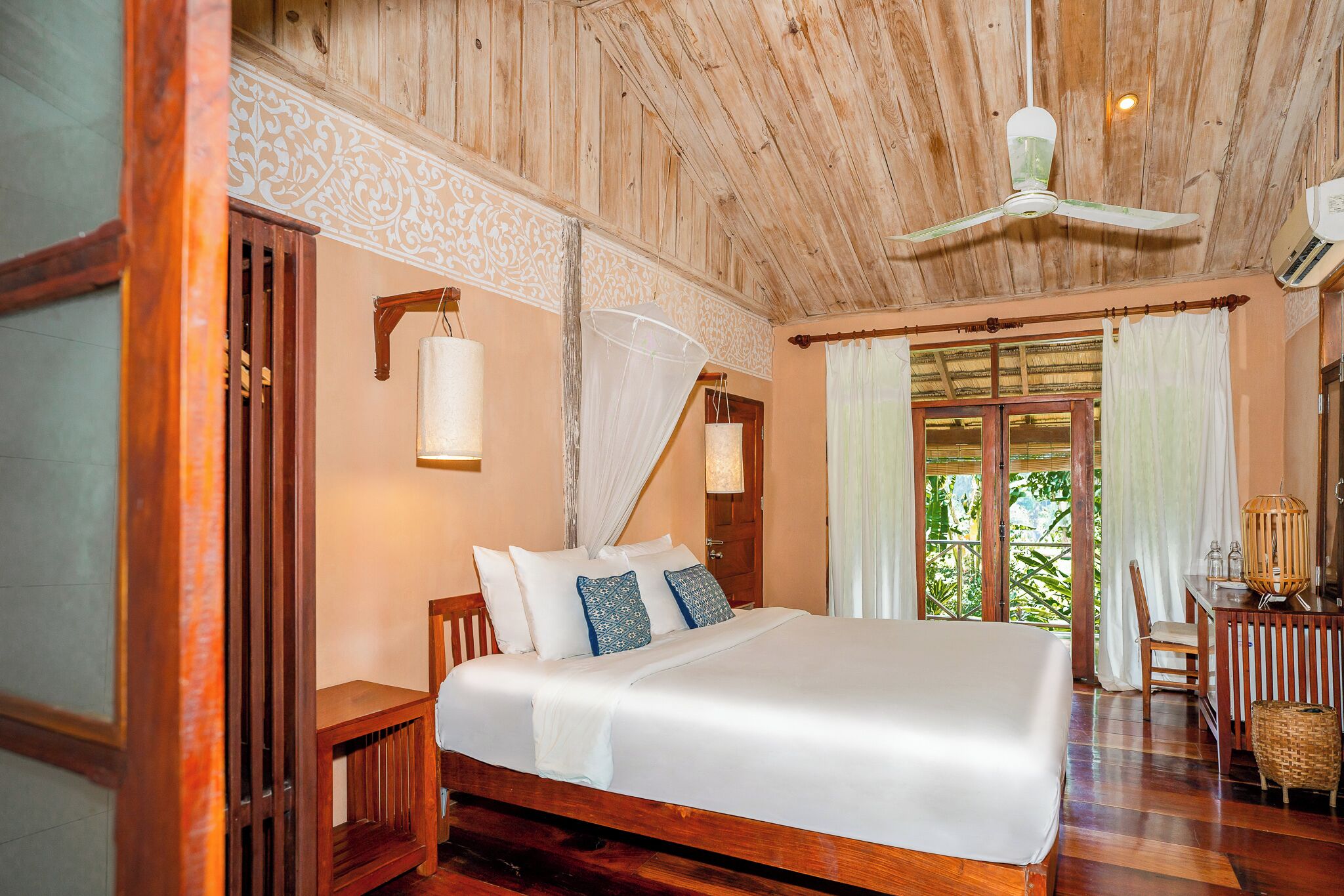 Ruime slaapkamer met een groot bed, houten plafond en uitzicht op groen.