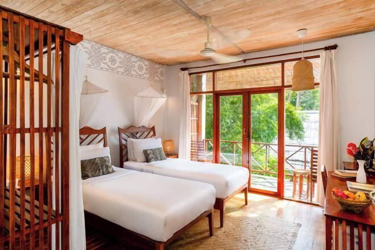 Une chambre avec deux lits, un plafond en bois, un balcon avec vue et un coin repas comprenant une table et des chaises.