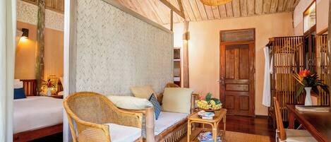 A cozy room with a bed, two wicker chairs, a small table with a fruit bowl, and a woven ceiling light.