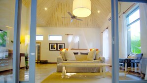 Un salón espacioso con un sofá grande, un ventilador de techo y vistas al exterior a través de amplias ventanas.