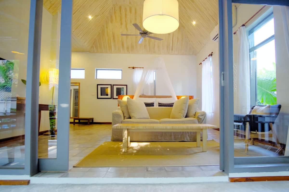 Un salon spacieux, doté d’un grand canapé, d’un ventilateur de plafond et offrant une vue sur l’extérieur grâce à de grandes fenêtres.