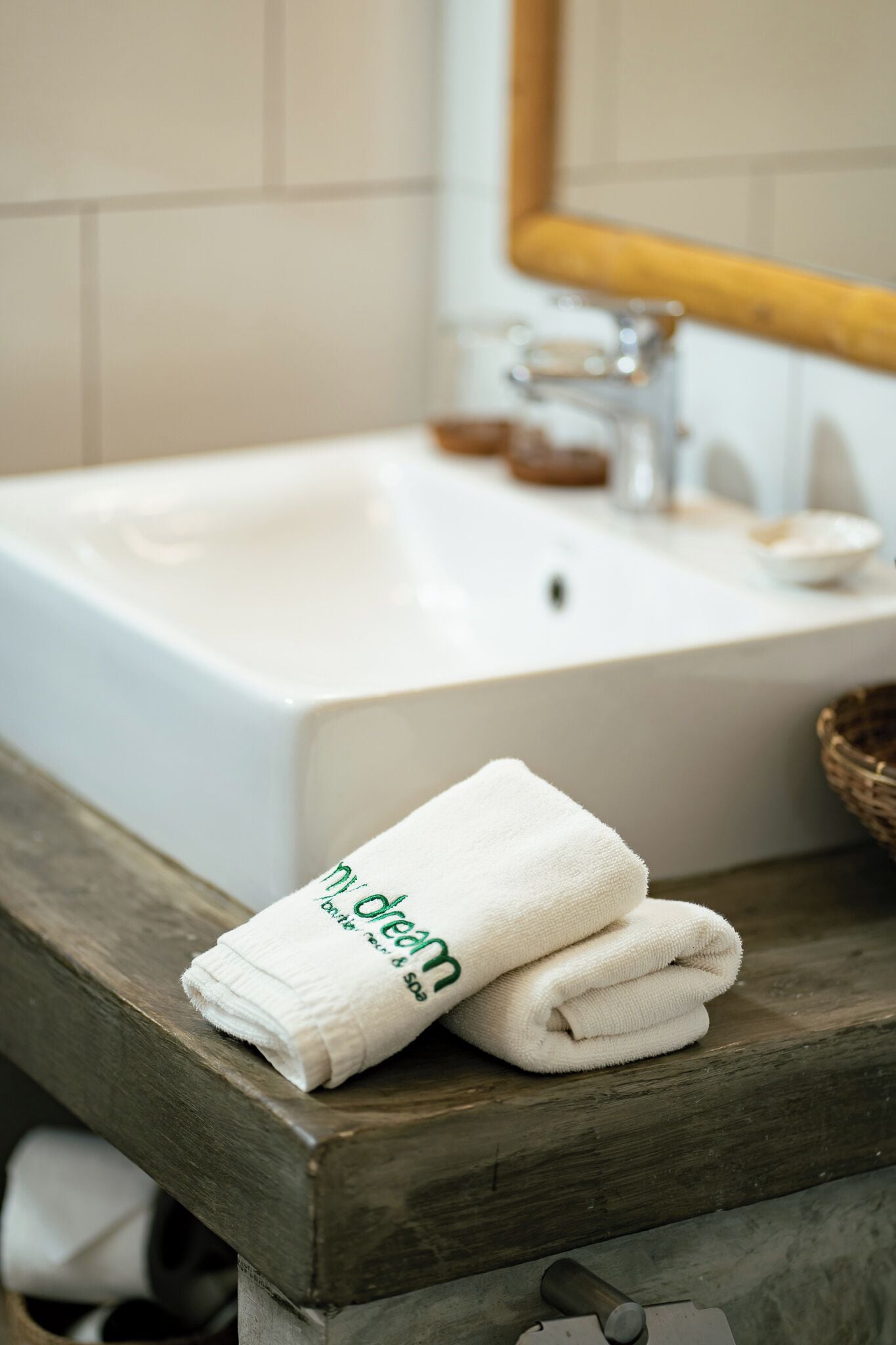Un baño con un lavamanos blanco, un banco de madera y una toalla con el texto 'dream'.