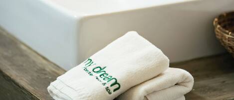 Un baño con un lavamanos blanco, un banco de madera y una toalla con el texto 'dream'.