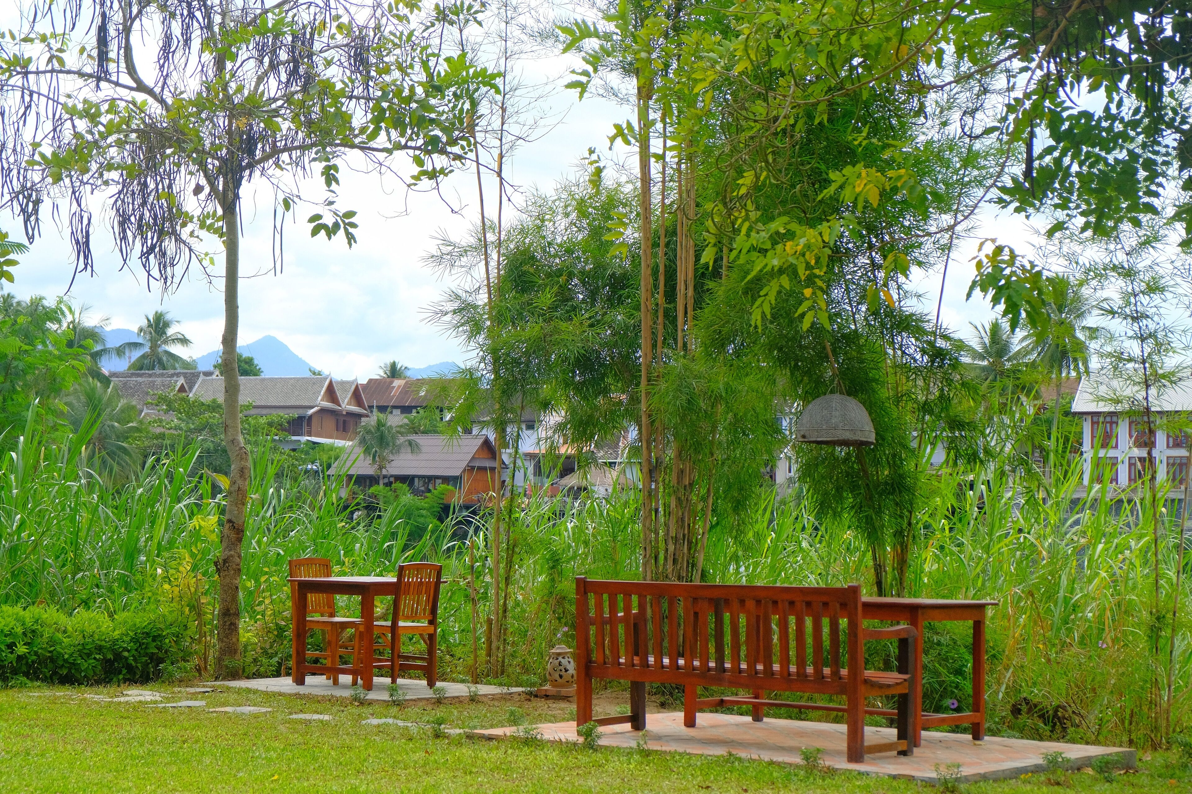 A wooden bench and chair in a lush garden with a view of traditional buildings in the background.