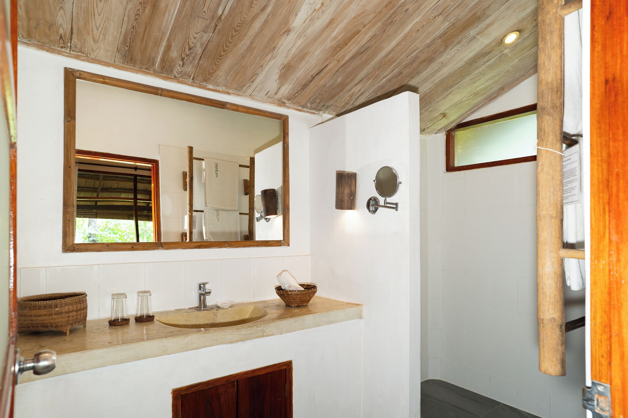 A bathroom with a wooden ceiling, a large mirror, a sink with a basin, and a shower area.