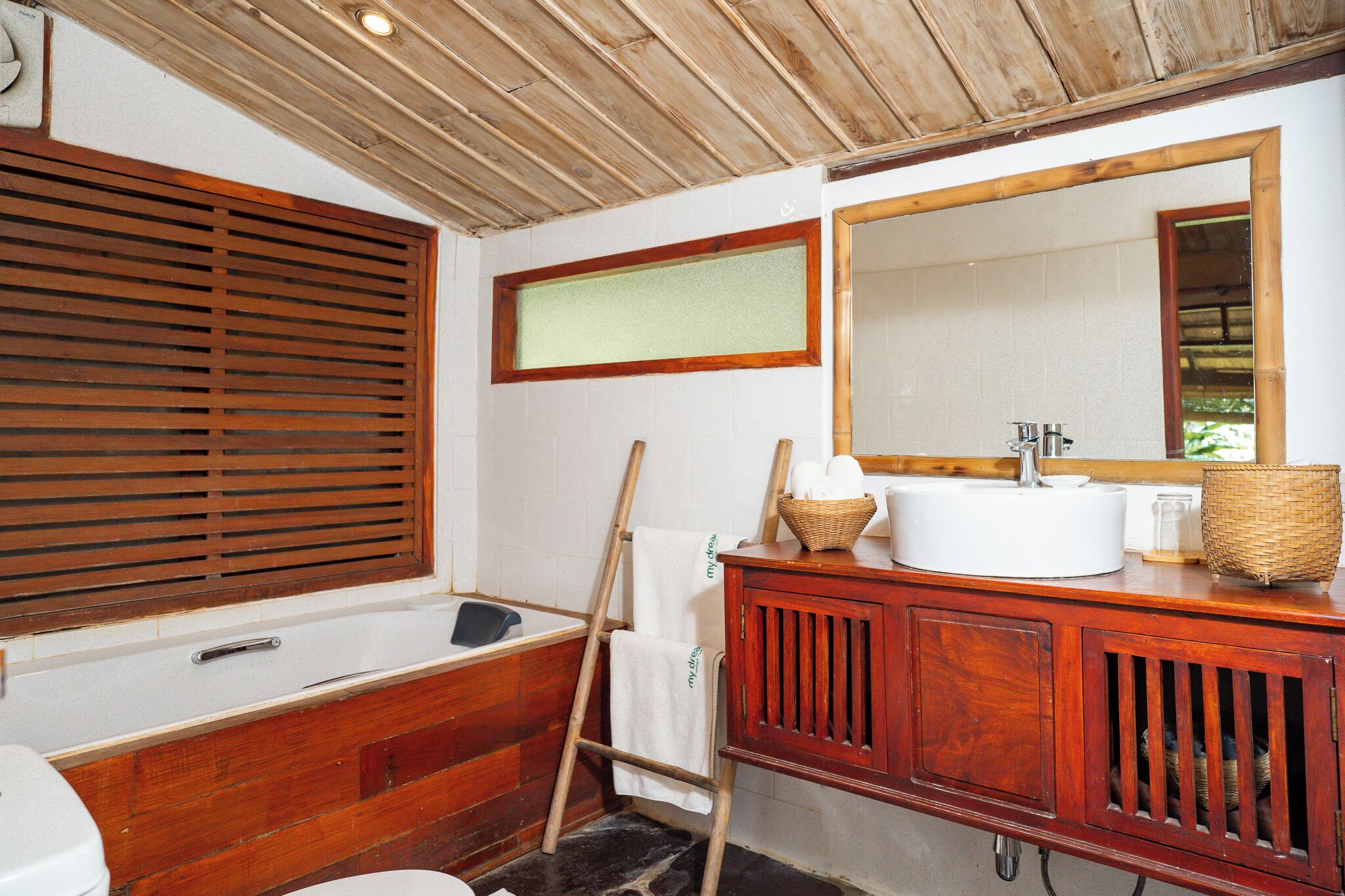 Un baño de madera con bañera, un espejo grande y un tocador de madera.