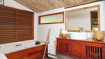 Un baño de madera con bañera, un espejo grande y un tocador de madera.